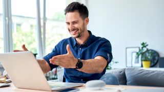 A man sitting in front of his laptop with his hands outstretched and a big smile on his face.