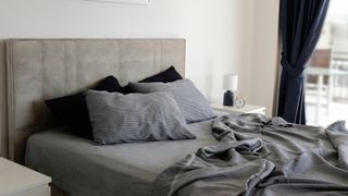 A king mattress covered in grey sheets placed on a grey bed