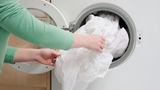 A woman places a waterproof mattress protector in a washing machine