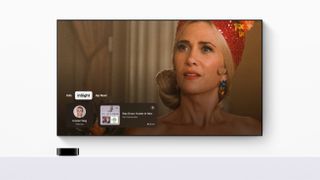 Apple TV on a grey surface with a TV above and actress Kristen Wiig on screen