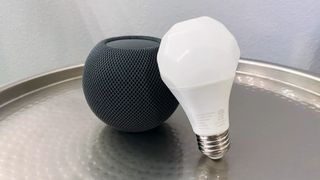 Nanoleaf Esssentials A19 Light Bulb leaning on a Space Gray HomePod mini