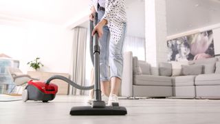 A young moan using a cylinder vacuum to clean hard floors in her home