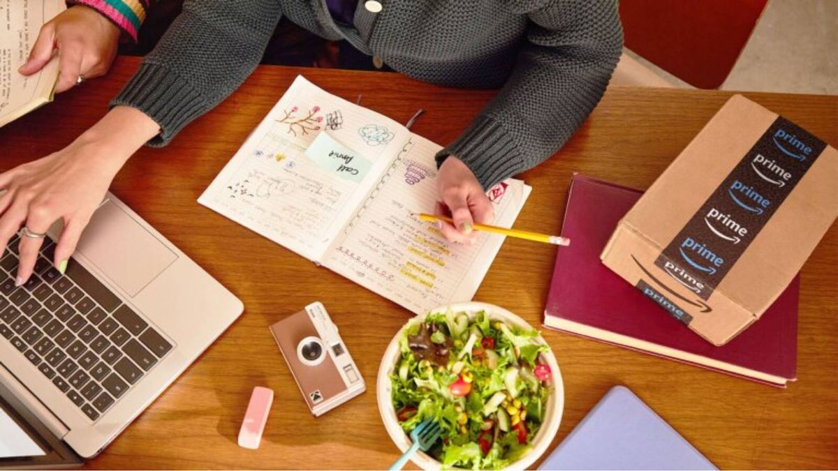 Amazon-back-to-school sale, student at desk typing on a laptop and writing in a notebook next to an Amazon prime box