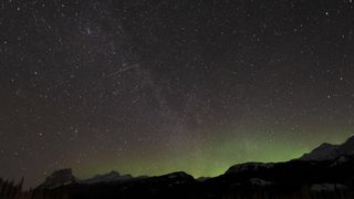 During the Quadrantid meteor shower a meteor streaks across the star-studded sky with mountains below.