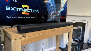 A 3/4 angle view of a black Sonos Arc soundbar on a TV cabinet in front of a TV showing the Extraction 2 title with the Netflix logo in the corner.