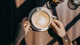 Top view of woman sitting by the window in coffee shop enjoying the warmth of sunlight and drinking coffee