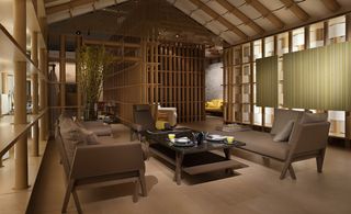 Inside the Pavillion Hermès structure. A lounge area with brown sofa's, a brown chair, a coffee table and a potted plant.