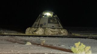 a scorched gray cone-shaped capsule sits on desert sand surrounded by scrub plants