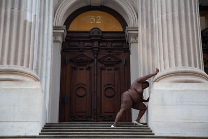 Nona Faustine artwork: black woman standing alone, pushing column of courthouse in New York