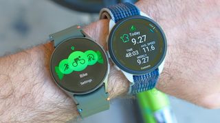 Close up of a Samsung Galaxy Watch 7 and Garmin Forerunner 165 on a user's wrist next to each other with a lime green bike in the background