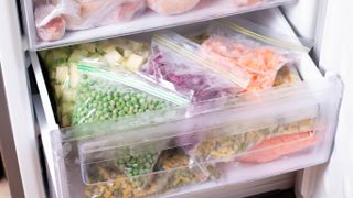 An open freezer drawer showing frozen vegetables in sealed bags