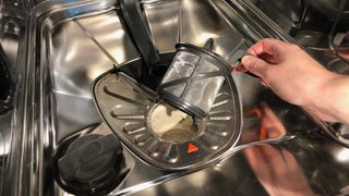 A dishwasher filter being lifted by hand from a dishwasher and inspected