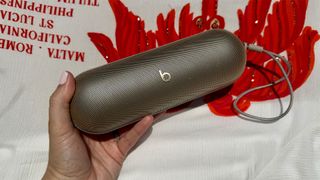 Beats Pill Bluetooth speaker held in hand in front of red and white graphic backdrop