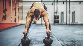 Man holding two kettlebells on the floor bending over during kettlebell workout outdoors