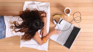 A woman laying on the floor and using a computer while drinking a coffee