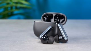 a pair of silver and black shiny earbuds with a black matte charging case are photographed against the Tom's Guide blue background