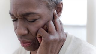 close up of a woman's face as she winces and holds a finger to one ear, as if trying to tune out a noise