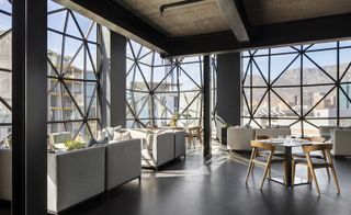 Lounging area of the restaurant with grey sofa and cushions, with a view of outside through a glass windows