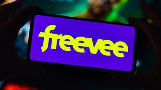 A phone with the &#039;freevee&#039; logo is held by two hands in the dark.