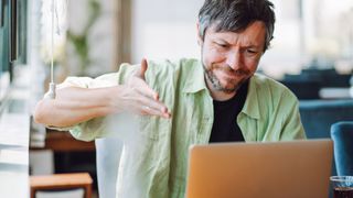 A man gesturing in a frustrated manner towards his laptop