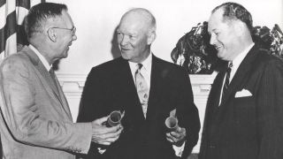 three men in suits smile at one another