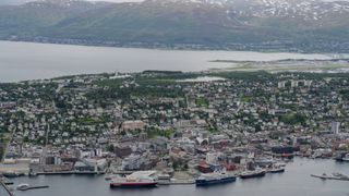 an aerial view of a cityscape with various ships in port the hurtigruten ship is white with black and red.
