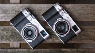 Fujifilm X100VI camera next to a Fujifilm X100V camera on a slatted wooden bench