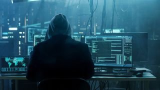 A hacker with a hood up looking at a computer screen.