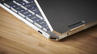 The Spectre x360 on a wooden desk showing off its ports, its hinge, and part of its keyboard