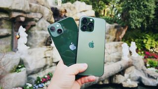 Green iPhone 13 and Alpine Green iPhone 13 Pro held in hand in front of Snow White fountain at Disneyland, CA