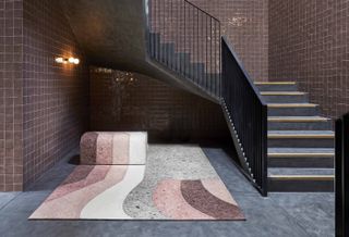 A striped rug in pink, purple and grey placed on the floor near a staircase with purple tiles on the walls