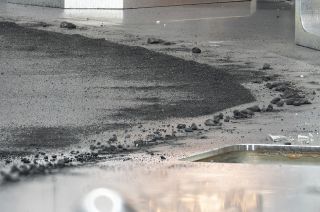 photo of dark powder and small dark pebbles on a silver metallic surface.