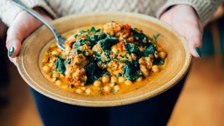 Person holding a plate containing a spinach and chickpea curry with tomatoes and spices