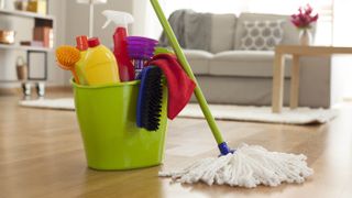 A mop and bucket filled with cleaning products on the floor of a living room with a couch and table in the background