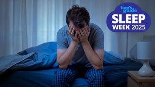 A man in a blue t shirt holds his head in his hands and sits on the edge of his bed because he can't sleep due to intrusive thoughts and needs to try cognitive shuffling for sleeping