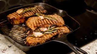 Three large steaks cooking in a cast iron skillet with garlic and rosemary on the top