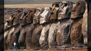 A woman looks at a row of massive stone statues.