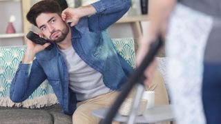 Man on sofa blocking ears from loud vacuum cleaner