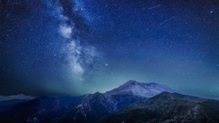 A photo of a meteor shower over a mountain range, with the Milky way visible