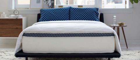 The WinkBed Mattress placed iagainst a winfow in a light an airy bedroom. On top of the bed is a white comforter and two pillows