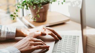 Woman working at home office with her hand on keyboard. Laptop is on a wooden desk