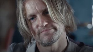 A close up of Woody Harrelson as Haymitch with hair in his face, he's smirking in The Hunger Games.