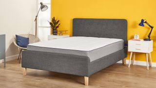 The Nectar Memory Foam Mattress shown on a grey fabric bed and placed against a bright yellow wall