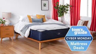 Cyber Monday mattress deals image shows the The DreamCloud Hybrid Mattress placed on a wooden bedframe in a bedroom with red curtains, and with a blue Cyber Monday mattress badge overlaid on the image