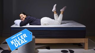 A woman wearing gray jogging bottoms and black jumper lays on her stomach on top of the Helix Midnight Luxe, which is 30% off in the 4th of July mattress sales