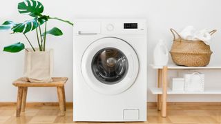 A washing machine next to detergent, a laundry hamper and a plant