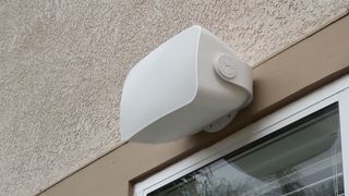 A Sonos custom install speaker mounted on an exterior wall above a window.