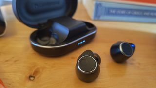 Cambridge Audio Melomania M100 wireless earbuds in front of case on wooden table