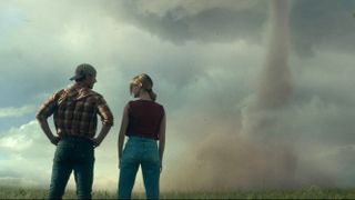 Glen Powell and Daisy Edgar-Jones facing away from the camera looking at a Tornado in &quot;Twisters&quot;