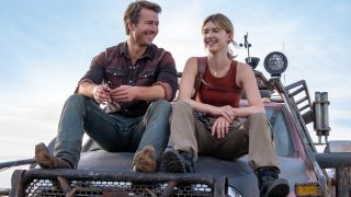 Glen Powell and Daisy Edgar-Jones smiling together while sitting on top of a truck's hood in Twisters.